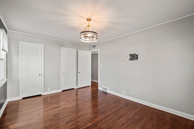 unfurnished bedroom featuring a notable chandelier, crown molding, and dark hardwood / wood-style floors