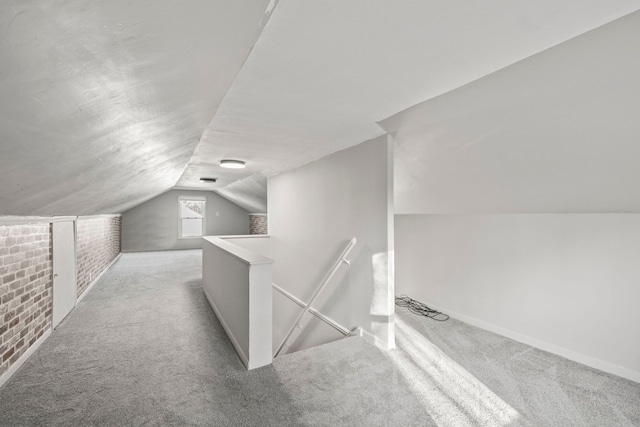 additional living space with brick wall, lofted ceiling, and light colored carpet