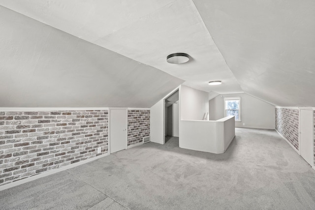 bonus room featuring vaulted ceiling, light colored carpet, and brick wall