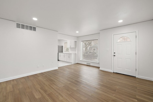 unfurnished living room with wood finished floors, visible vents, and baseboards