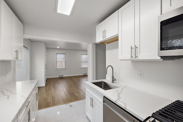 kitchen with light stone countertops, appliances with stainless steel finishes, white cabinets, and a sink