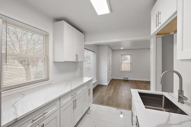 kitchen with light stone countertops, baseboards, white cabinets, and a sink