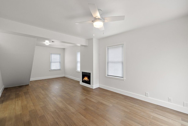 unfurnished living room featuring a ceiling fan, baseboards, a lit fireplace, and light wood finished floors