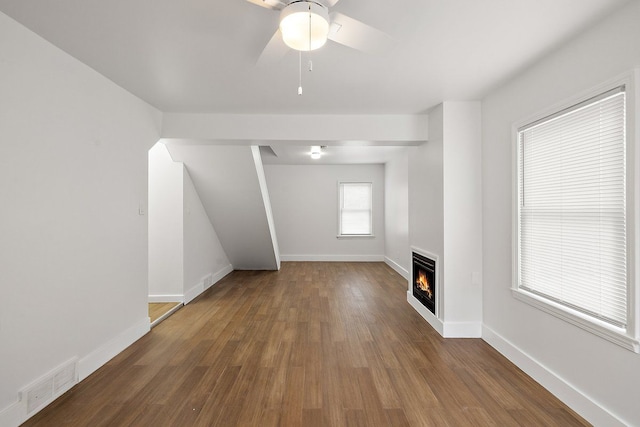 unfurnished living room featuring a warm lit fireplace, dark wood-type flooring, visible vents, baseboards, and heating unit