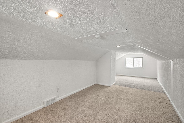 bonus room featuring carpet floors, visible vents, a textured wall, vaulted ceiling, and a textured ceiling