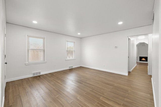 unfurnished room featuring visible vents, a lit fireplace, baseboards, and wood finished floors