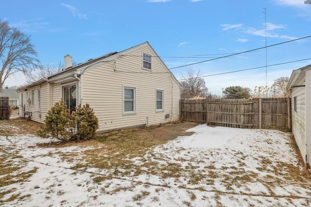 snow covered back of property featuring a chimney and fence