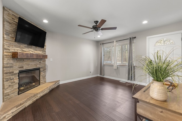 living room with a stone fireplace, dark wood-type flooring, and ceiling fan