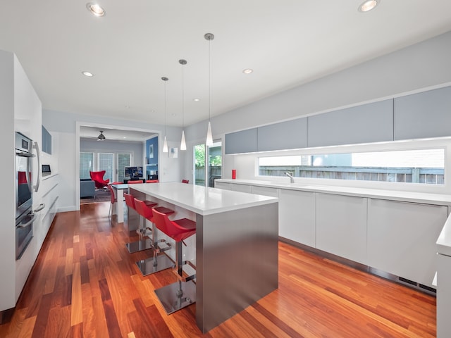 kitchen featuring a kitchen island, white cabinetry, a breakfast bar area, hanging light fixtures, and light wood-type flooring
