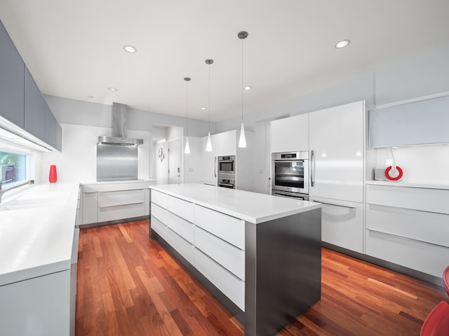 kitchen featuring white cabinetry, wood-type flooring, hanging light fixtures, a center island, and exhaust hood