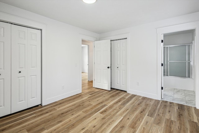 unfurnished bedroom with ensuite bathroom, light hardwood / wood-style floors, and two closets