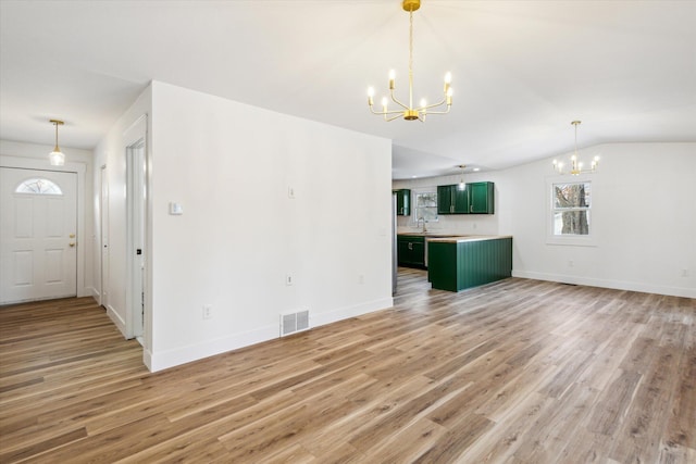 unfurnished living room with vaulted ceiling, a notable chandelier, and light wood-type flooring