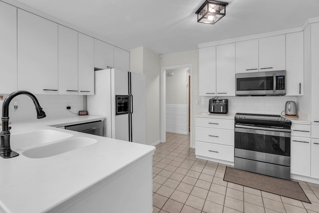 kitchen with sink, tasteful backsplash, light tile patterned floors, appliances with stainless steel finishes, and white cabinets