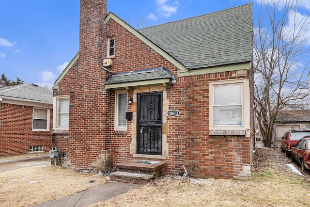 view of front facade featuring brick siding, roof with shingles, and a chimney