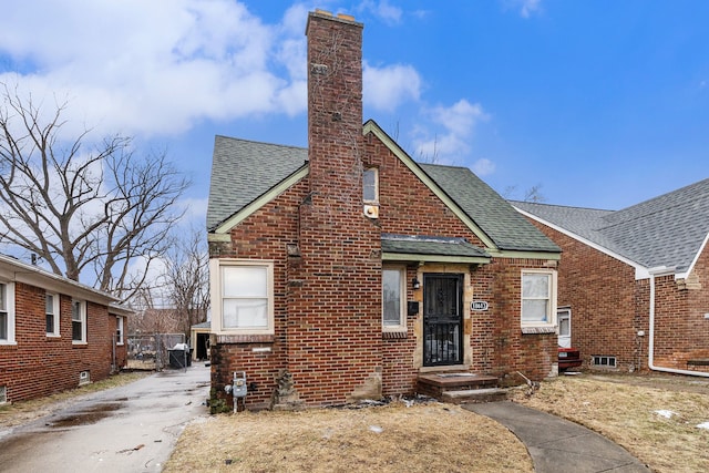 bungalow-style house with a shingled roof, a chimney, and brick siding