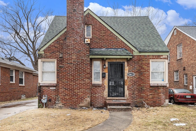 bungalow-style home featuring brick siding, a chimney, and roof with shingles