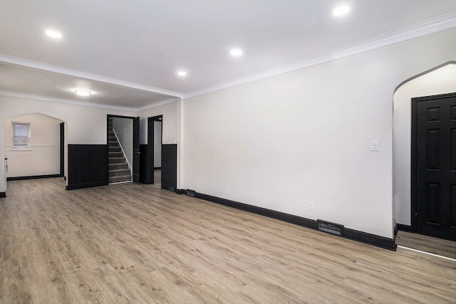 interior space featuring arched walkways, baseboards, light wood-style flooring, stairway, and crown molding