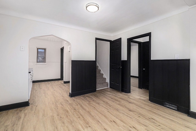 empty room featuring stairs, wainscoting, light wood-type flooring, and arched walkways