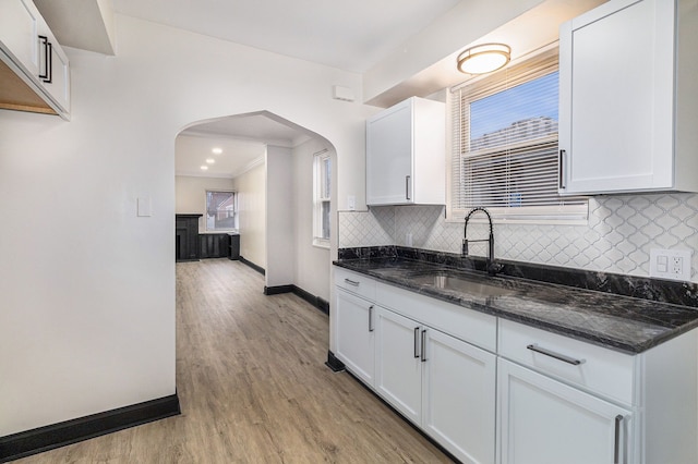 kitchen with arched walkways, light wood-style flooring, decorative backsplash, a sink, and dark stone countertops