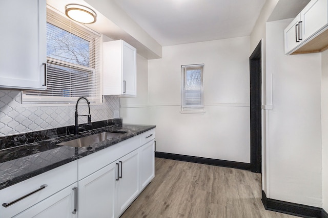 kitchen with dark stone counters, a sink, white cabinetry, and light wood-style floors