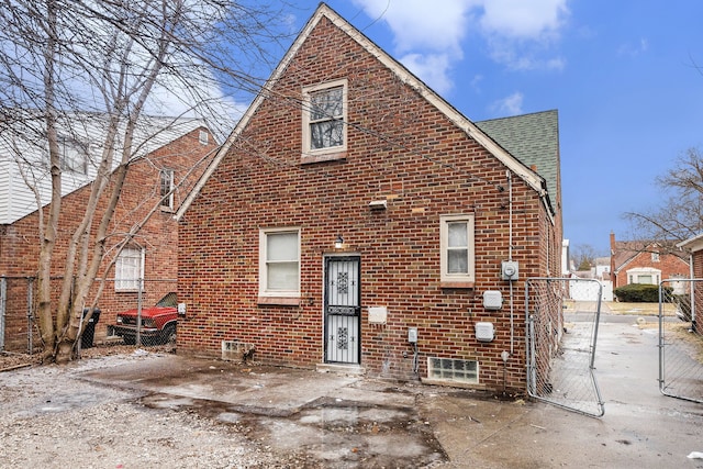 view of front of house with a gate, brick siding, fence, and roof with shingles