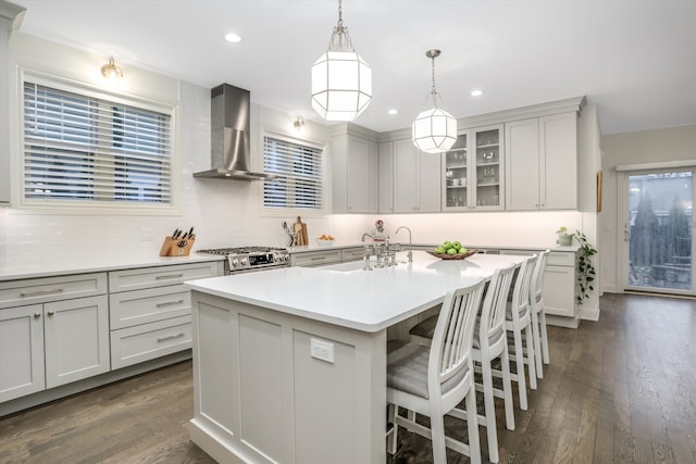 kitchen with decorative light fixtures, sink, a center island with sink, stainless steel range oven, and wall chimney exhaust hood