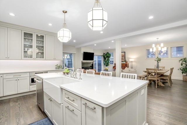 kitchen featuring white cabinetry, stainless steel dishwasher, dark hardwood / wood-style flooring, an island with sink, and pendant lighting