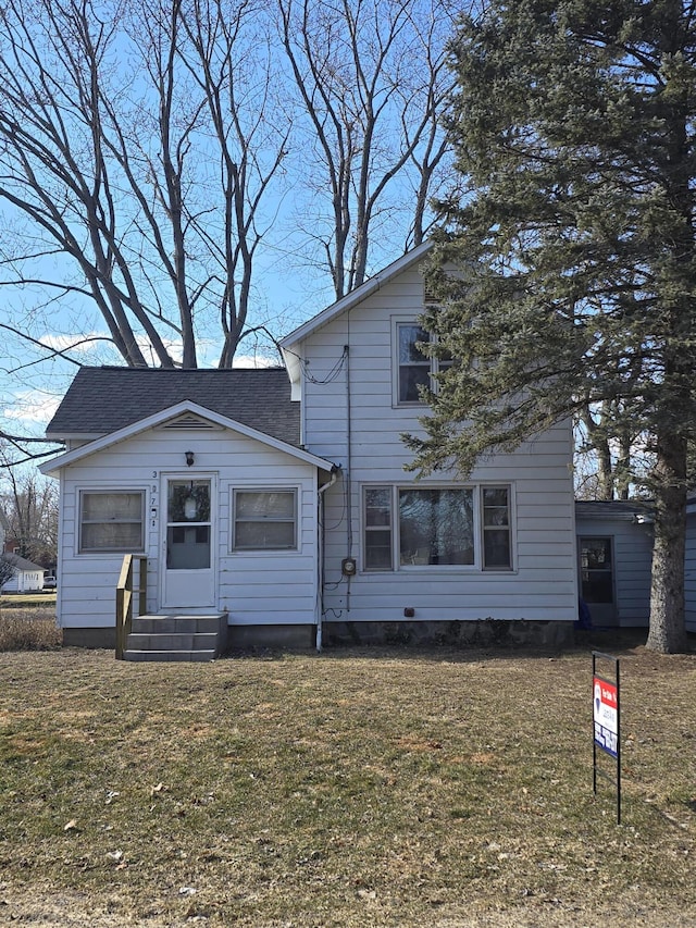 traditional home featuring entry steps, a shingled roof, and a front yard