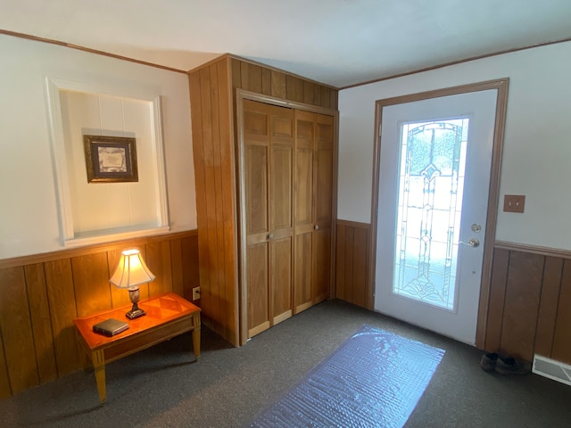 entryway featuring ornamental molding, dark colored carpet, and wood walls