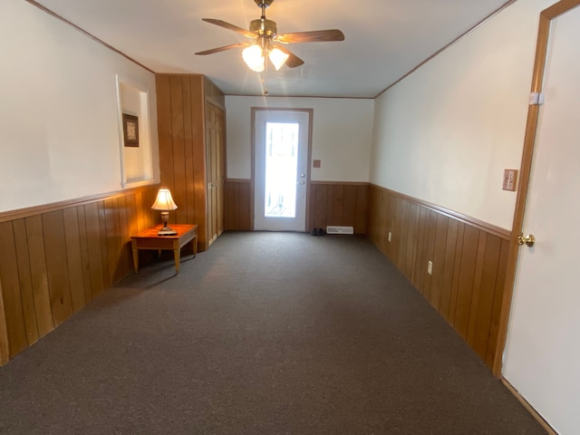 carpeted spare room featuring wooden walls and ceiling fan