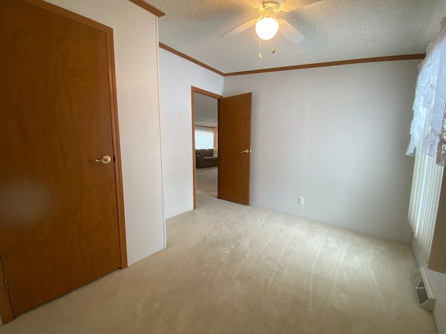 carpeted spare room with ceiling fan, crown molding, and a textured ceiling