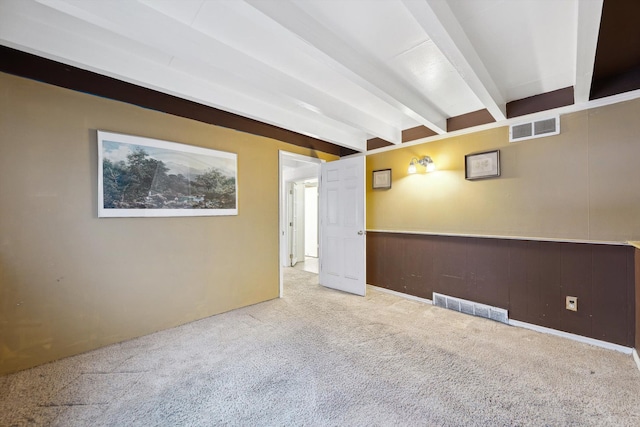 empty room featuring light colored carpet, beam ceiling, and wood walls