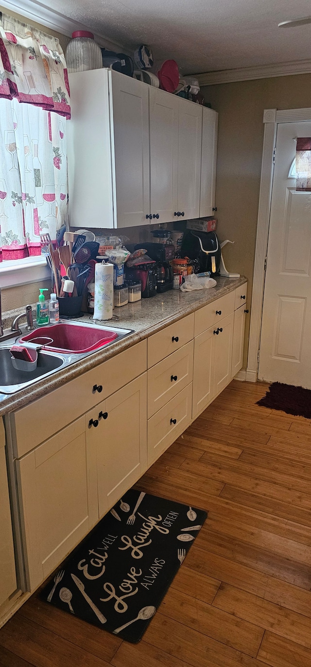 kitchen featuring white cabinetry, ornamental molding, dark hardwood / wood-style flooring, and sink