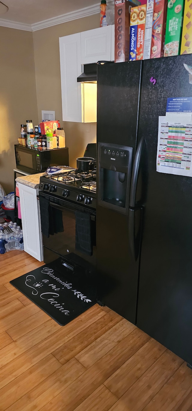 kitchen with hardwood / wood-style floors, crown molding, black appliances, and white cabinets