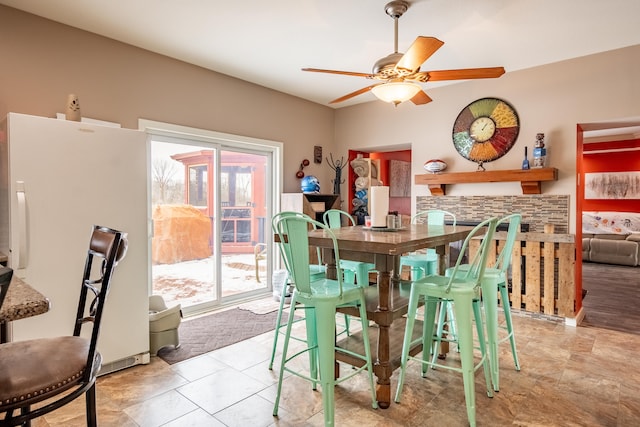 dining area featuring ceiling fan and a stone fireplace