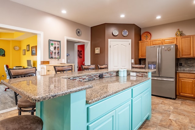 kitchen featuring a kitchen island, tasteful backsplash, stainless steel fridge, a kitchen breakfast bar, and light stone countertops