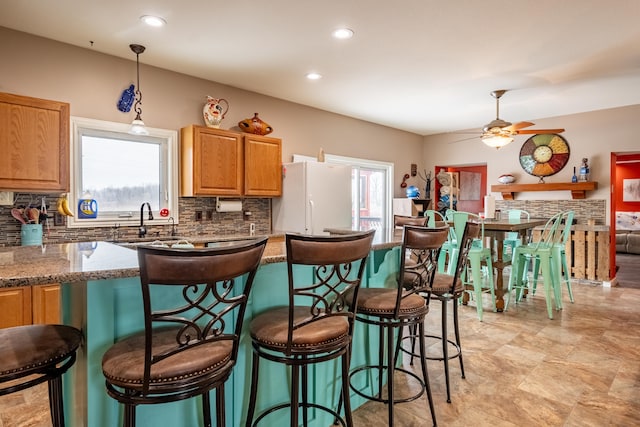 kitchen with hanging light fixtures, plenty of natural light, stone countertops, and white fridge