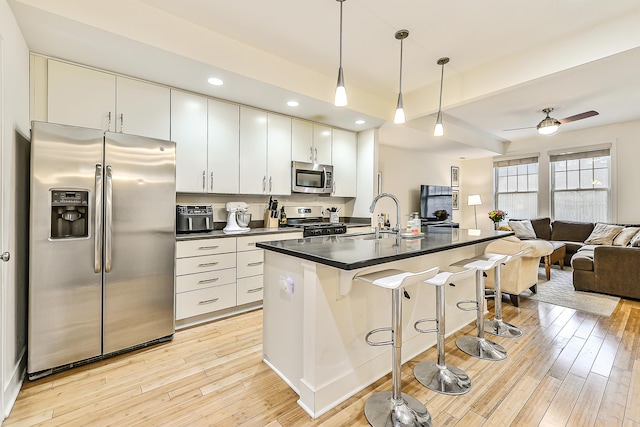 kitchen with pendant lighting, white cabinetry, stainless steel appliances, a kitchen breakfast bar, and an island with sink