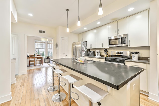 kitchen featuring pendant lighting, white cabinetry, stainless steel appliances, a center island with sink, and light hardwood / wood-style flooring