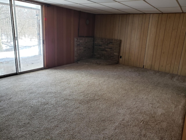 interior space with a drop ceiling, carpet floors, and wood walls