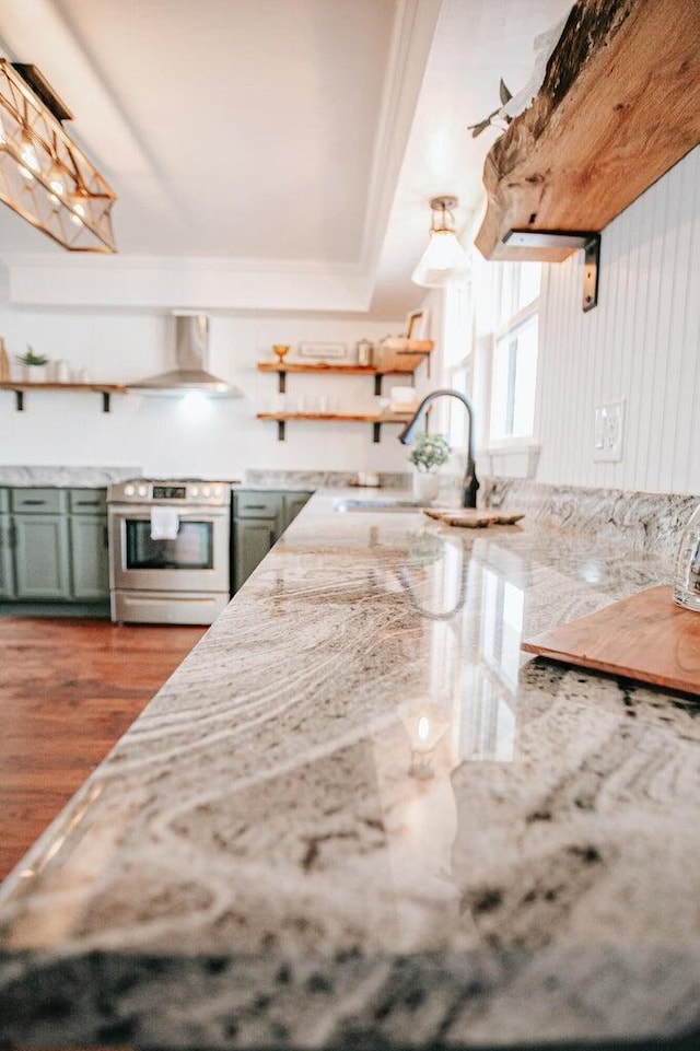 kitchen with electric stove, sink, hardwood / wood-style flooring, green cabinets, and wall chimney exhaust hood