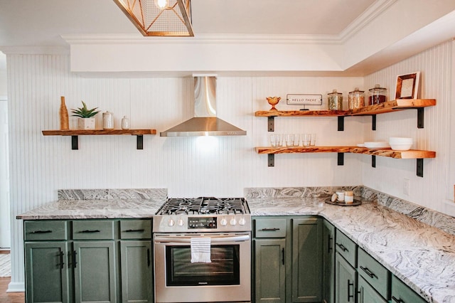 kitchen with wall chimney range hood, stainless steel gas range, green cabinets, ornamental molding, and light stone countertops