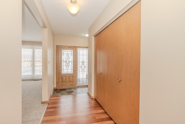 foyer featuring light wood finished floors, baseboards, and light colored carpet