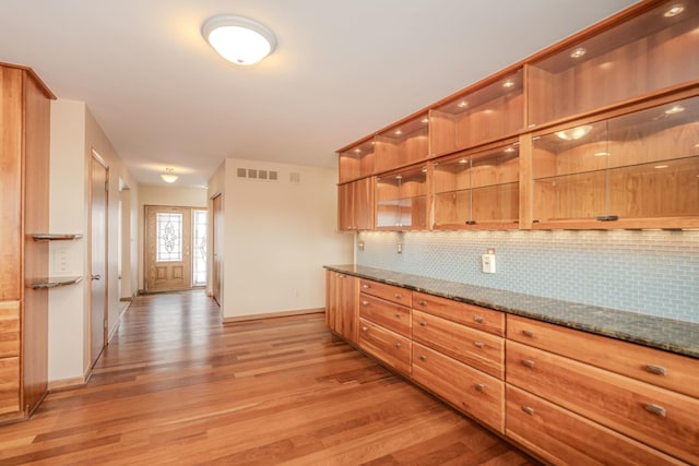 kitchen with light wood-style floors, dark stone countertops, baseboards, and backsplash