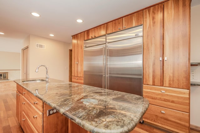 kitchen with visible vents, built in refrigerator, stone counters, a sink, and recessed lighting