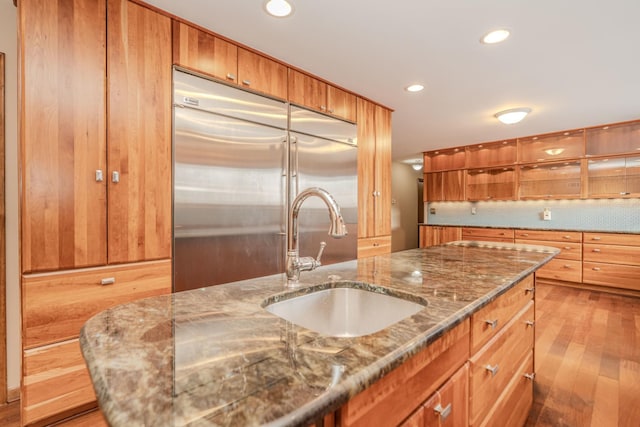 kitchen with recessed lighting, decorative backsplash, a sink, wood finished floors, and stainless steel built in refrigerator