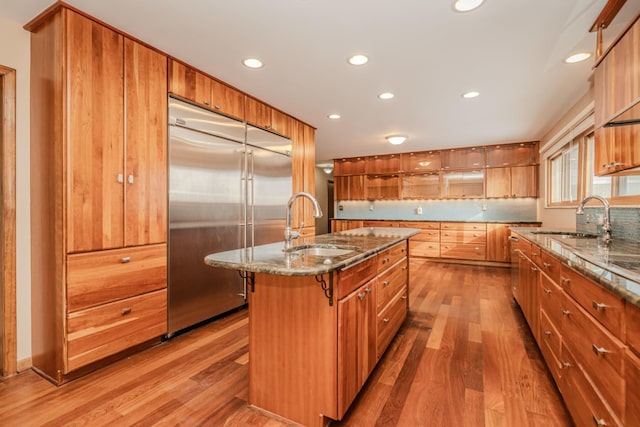 kitchen featuring built in refrigerator, dark stone countertops, and a sink