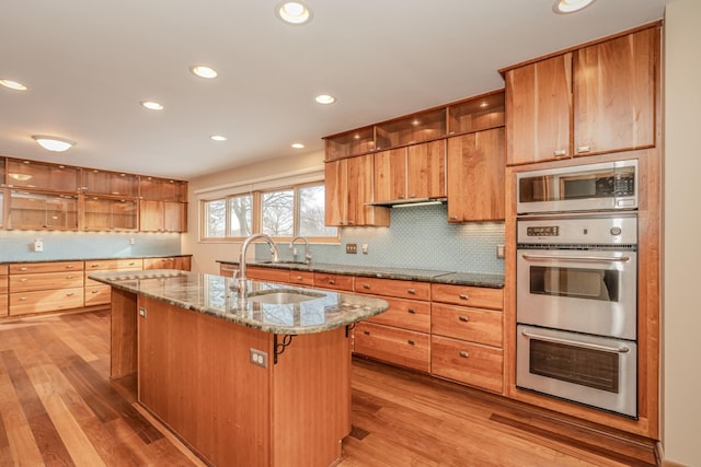 kitchen with appliances with stainless steel finishes, stone countertops, a sink, and light wood-style floors