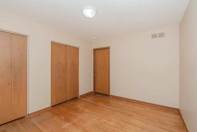 unfurnished bedroom featuring light wood finished floors, two closets, visible vents, and baseboards