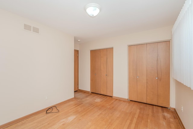 unfurnished bedroom with multiple closets, light wood-type flooring, visible vents, and baseboards